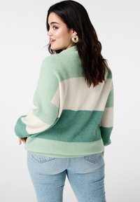 Pull tricot rayé vert et crème à coupe décontractée, avec une texture côtelée et des manches longues, associé à un jean denim bleu clair.