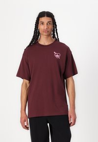 Mørkerød bomulds t-shirt med rund hals og korte ærmer. Har et pink hjerte-logo på venstre bryst. Løs pasform.