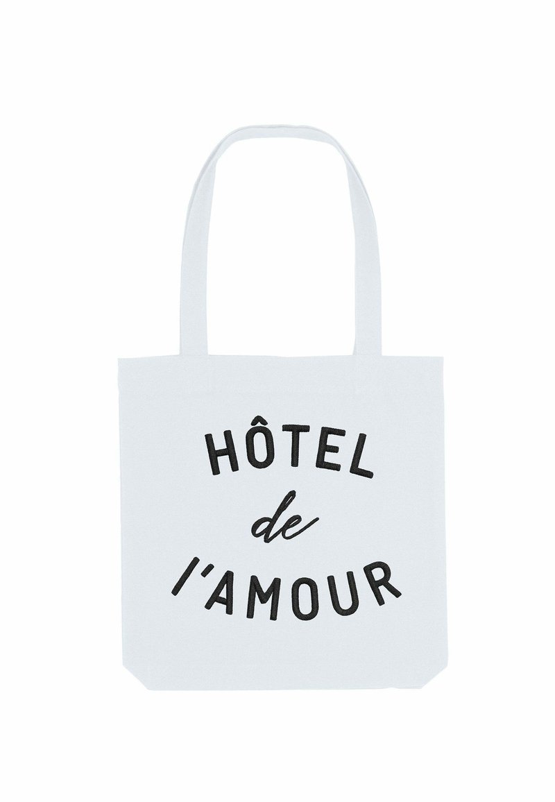 Borsa in cotone bianca con testo nero che recita "HÔTEL de l'amour." Presenta due manici robusti e un design spazioso.