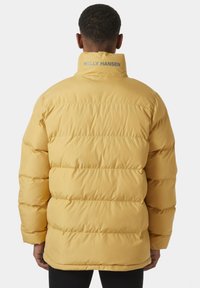 Žlutá prošívaná bunda s horizontálním švem, vysokým límcem a logem "HELly HANSEN" na zadní straně. Hladký povrch, navržena pro teplo.