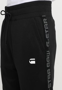 Černé bavlněné jogger kalhoty s elastickým pasem, šnůrkou, bočními kapsami a potiskem šedého loga "G-STAR RAW" na boku.