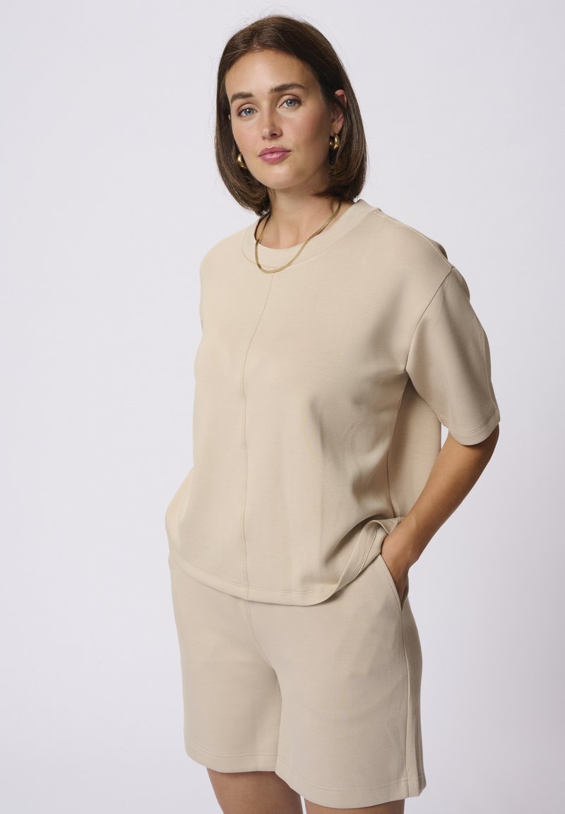 Ensemble bi-matière beige clair composé d'un haut à manches courtes au fit décontracté avec poches latérales, associé à un short assorti. Texture lisse.