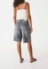 Zwarte vervaagde denim short met een losse pasvorm, omgeslagen zomen en klassieke achterzakken. Draag ze met een wit, uitgerafeld cropped topje.