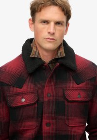 Rød og sort ternet flannel jakke med en sort, blød krave, forlommer og knaplukninger, med et struktureret, tykt stof.