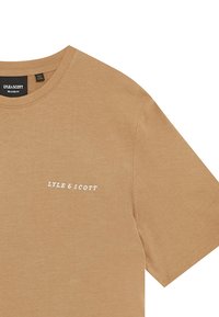 Beige bomullströja med avslappnad passform, med rund hals och vitt tryckt logotyp "LYLE & SCOTT" på vänster bröst.
