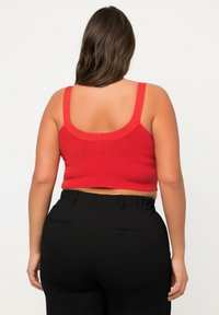 Rotes geripptes Crop-Top mit breiten Schulterträgern, kombiniert mit schwarzen hochtaillierten Hosen mit flachem Bund und seitlichen Taschen.