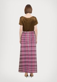 Top satin marrone con scollatura ampia, abbinato a una lunga gonna a scacchi rosa con strisce orizzontali e verticali.