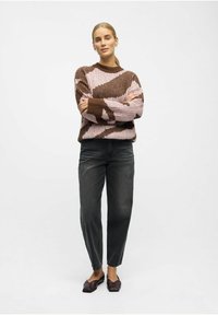 Pull en tricot avec des rayures brunes et roses, associé à un jean noir. Le pull présente une texture côtelée et une encolure ronde. Chaussures marron à bout carré.