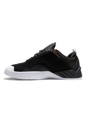 Svart sneaker laget av semsket skinn og syntetiske materialer, med såle i hvitt gummi, teksturerte sider og gull detaljer på hælen.