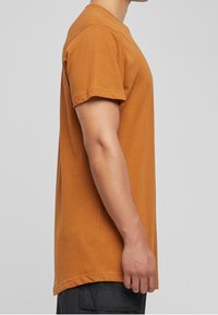 Kurzärmliges T-Shirt in einer einheitlichen Rostfarbe, aus weicher Baumwolle, mit lockerer Passform, rundem Ausschnitt und geradem Saum.