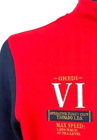 Felpa con zip rossa e blu navy, con alto collo. Presenta ricami bianchi che leggono "Ghedi VI" e testo aggiuntivo sul petto e sulla manica.