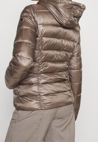 Hnědá péřová bunda s kapucí, se sp horizontalním prošíváním, lesklou texturou a zlatými kovovými akcenty. Nositelná s kostkovanými kalhotami.