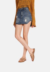 Sandali piatti intrecciati in marrone chiaro, con una suola flessibile e design open-toe. Abbinati a una minigonna in denim invecchiato e a una maglia.