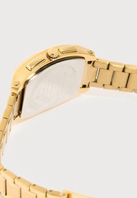 Orologio da polso in metallo color oro con cassa rettangolare, due pulsanti laterali e bracciale a maglie su sfondo bianco.