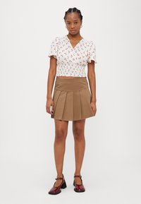 Hvit blomstret topp med korte puffermer, parret med en brun plissert skjørt og burgunder blokkhelede sko. Enkel design og tettsittende silhuett.