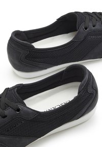 Schwarze Sportschuhe mit einem Obermaterial aus Netzgewebe, strukturierten Details und Schnürdesign. Weiße Gummisohlen bieten Kontrast und Unterstützung.