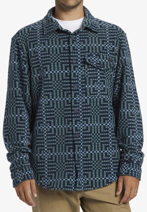 Chemise en flanelle à boutons avec un motif géométrique bleu et vert. Dispose de manches longues, d'une poche poitrine et d'un col. Fabriquée en tissu doux.