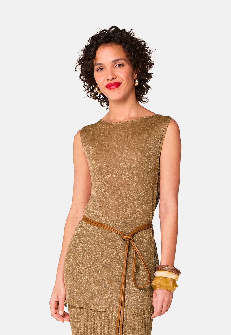 Metaalachtige gouden mouwloze gebreide top met een ronde halslijn, strakker getrokken op de taille met een bruine riem. Inclusief gelaagde, chunky armbanden om de pols.