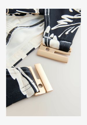 Schwarz-weiß gemusteter Stoff mit goldfarbigen Verschlüssen, zeigt glatte Textur und klare Linien.