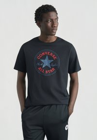 Μαύρο βαμβακερό μπλουζάκι με μεγάλο κυκλικό κόκκινο και μπλε λογότυπο Converse με αστέρι, συνοδευόμενο από μαύρο παντελόνι φόρμας που ταιριάζει.