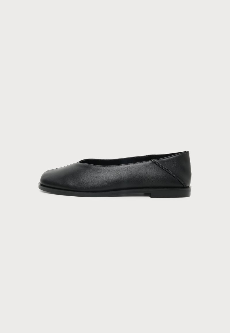Chaussure de ballet plate en cuir noir avec bout rond et petit talon, présentée en profil latéral sur un fond clair uni.