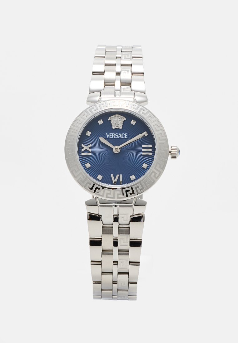 Montre en acier inoxydable argenté avec un cadran bleu rond, des détails décoratifs sur la lunette, des chiffres romains et un emblème de Versace en haut.