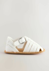 Vit sandal med flätade remmar och öppen tå. Har en silverfärgad spänne och en brun, strukturerad korkliknande sula.
