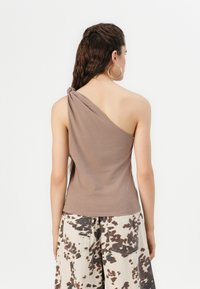 Top brown, cu un umăr, cu detaliu răsucit; material moale, ușor. Asortat cu pantaloni largi, cu model, în nuanțe de crem și maro.