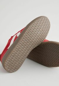 Czerwony płócienny sneaker z białymi akcentami, wyposażony w teksturowaną gumową podeszwy oraz wzór w plaster miodu dla lepszej przyczepności.