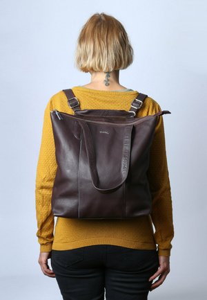 Braune Ledertasche mit zwei Schulterriemen, Reißverschlussdeckel und Seitentaschen, vor einem hellen Hintergrund abgebildet.