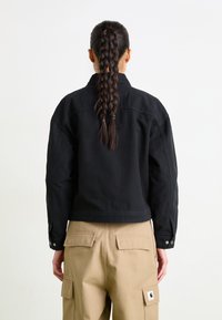 Zwarte denim jas met een cropped ontwerp, voorzien van knoopsluitingen en een losse pasvorm, gedragen over beige cargobroeken.