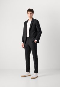 Črn suit z zareznimi reverji, slim fit hlače in bele majice pod kamizolo. Opremljen je z belimi supergami z gumijastim podplatom, gladko tkanino in minimalnim okrasjem.