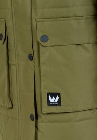 Olivgrön puffjacka med tryckknappar, med två framfickor med klaffar och en svart logotyp med texten "WHISTLER."