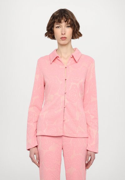 Blusa de manga larga con patrón floral en tonos rosas, cierre de botones y cuello tipo camisa. Fabricada en una tela texturizada.