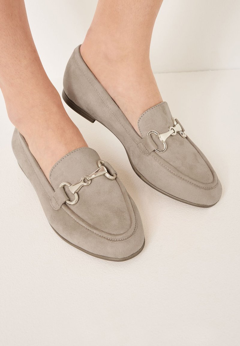 Grijze suède loafers met een spitse neus, voorzien van een zilveren metalen hardware detail over de bovenkant en een lage, platte hak.