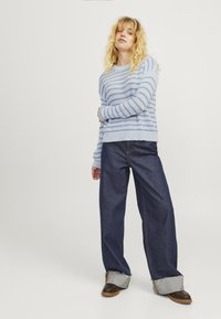 Világoskék csíkos pulóver, puha anyagból, laza sötét farmernadrággal és barna cipőkkel, szürke mandzsettával.