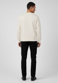 Felpa color crema, maniche lunghe, polsini e orlo a costine, texture liscia. Indossata con pantaloni neri a gamba affusolata e scarpe nere. Vista posteriore.