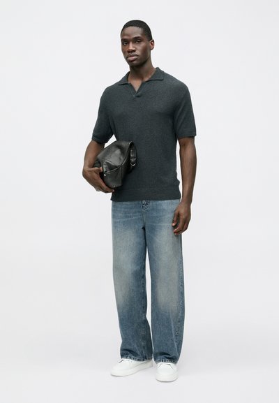 Σκούρο γκρι κοντομάνικο πόλο με γιακά, σε συνδυασμό με ανοιχτό μπλε τζιν φαρδιάς γραμμής και λευκά αθλητικά παπούτσια, κρατώντας μια μαύρη τσάντα.