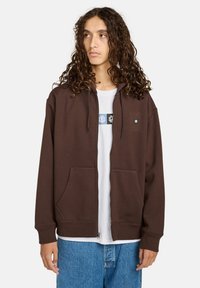 Bruine rits hoodie gemaakt van zachte stof, met een capuchon met trekkoord, voorzakken en een logo-detail op de borst.