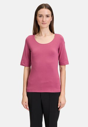 Top a maniche corte con scollo a barco in morbido tessuto rosa aderente, abbinato a pantaloni neri. Presenta una texture liscia e leggera.