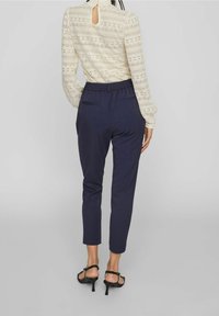 Navyhousut elastisella vyötäröllä, joissa on takataskut. Yhdistetty kermaiseen pitsipaitaan, jossa on monimutkaisia kuvioita ja avainaukkodetail.