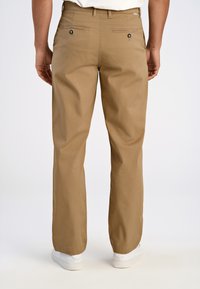 Beige casual broek met een rechte pasvorm, voorzien van twee achterzakken en metalen knopen, gecombineerd met witte sneakers op een effen achtergrond.