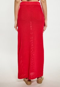 Rode gebreide maxirok, met een open geweven ontwerp, rechte silhouet en zijsplitten. Elastische tailleband en zachte textuur.