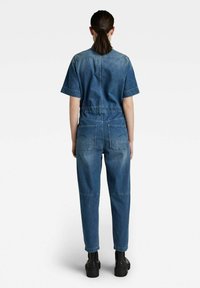 Dénim combinaison avec manches courtes, taille élastique et jambes droites. Dispose de deux poches arrière et d'une finition bleu délavé.