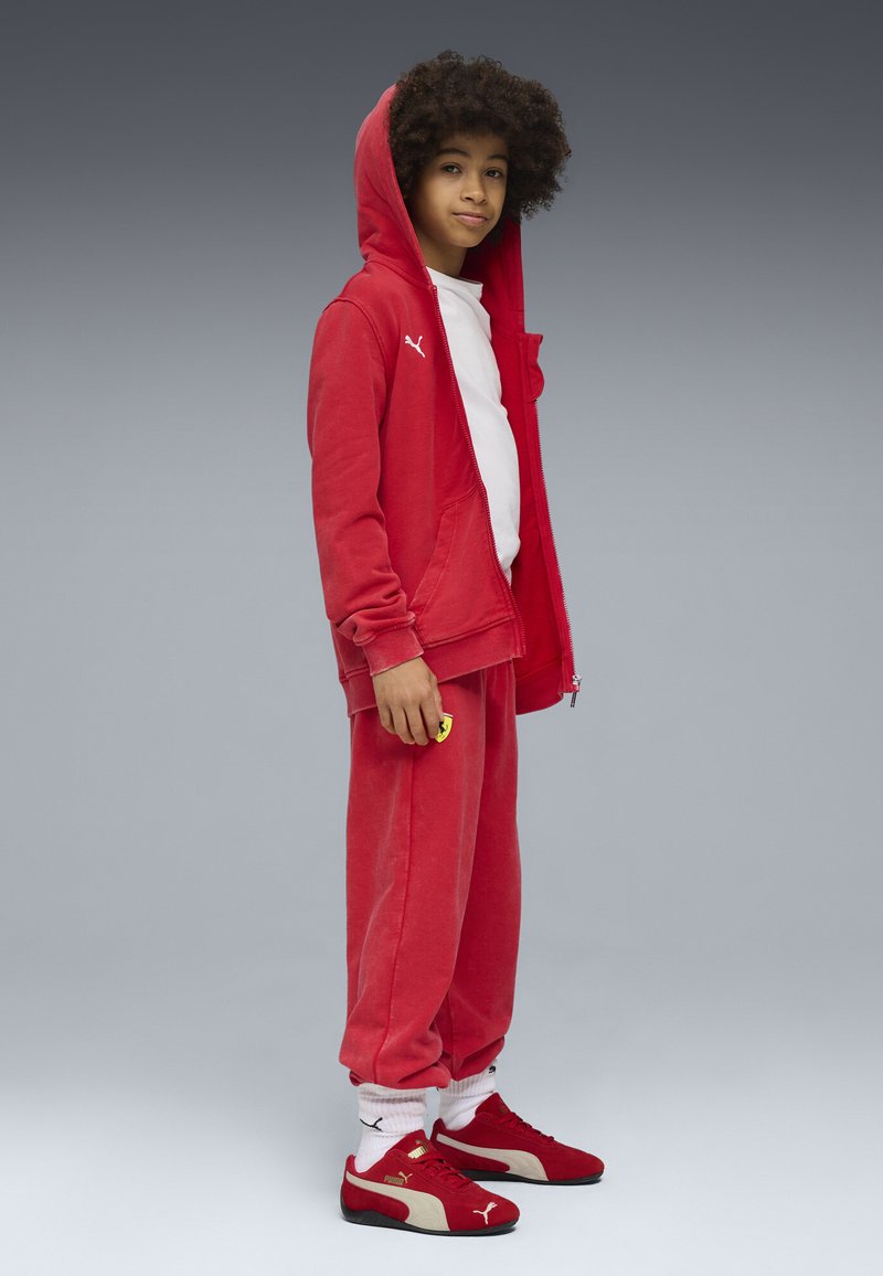 Roter Sweatshirt und Sweatpants aus weichem Material, mit einem weißen Logo und einem gelben Akzent. Rote Sneakers mit cremefarbenen Details und weißen Socken.