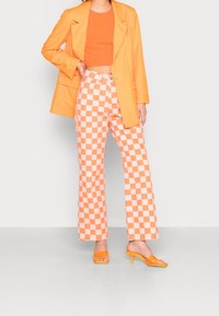 Oranger oversize Blazer über einem enganliegenden orangen Crop-Top, kombiniert mit karierten pinken und orangen Schlaghosen und orangefarbenen High Heels.