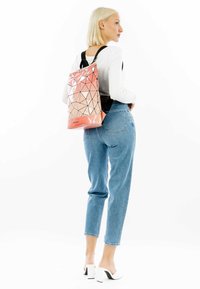 Rückansicht eines geometrisch gemusterten Rucksacks in Pink und Orange, aus glänzendem Material, getragen mit blauen Jeans und einem weißen Oberteil.