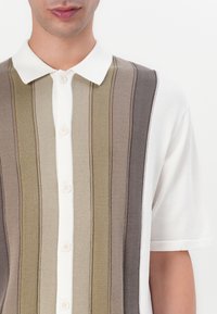 Kortermet polo skjorte med stripete design i beige, oliven og brune nyanser, med klassisk krage og knappestolpe. Glatt tekstur.
