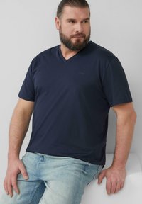 Marineblauwe V-hals t-shirt van gladde stof, met korte mouwen, voorzien van een subtiele logo-detail op de borst, gecombineerd met lichte spijkerbroeken.