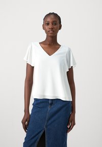 White, short-sleeved blouse with a V-neckline and soft, flowing fabric. Paired with a blue denim skirt featuring a front slit.